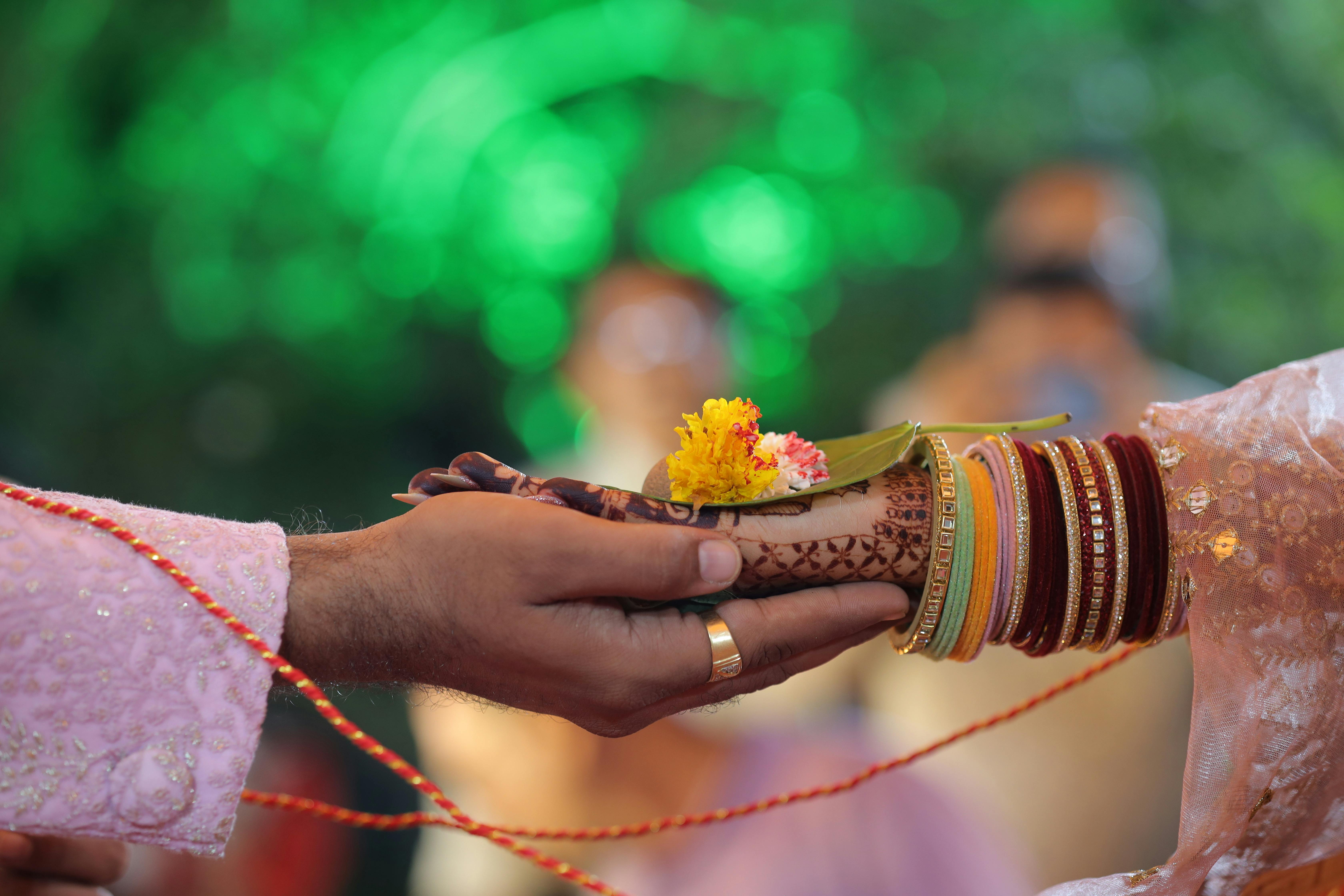 A couple's hennaed hands exchanging a flower offering during a wedding ritual